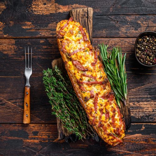 Baguette stuffed with ham, bacon, vegetables and cheese on wooden board.